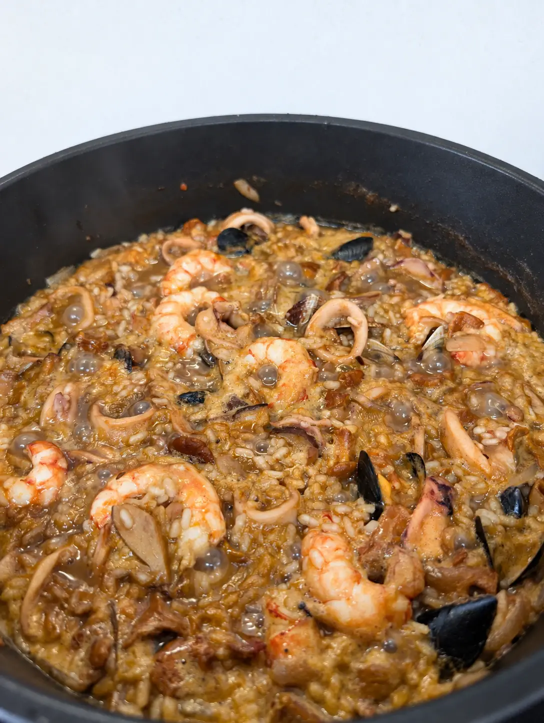 Arròs amb bolets i sípia en una cassola, encara bullint: arròs melós amb trossos de sípia, gambes, musclos, cloïsses i bolets.