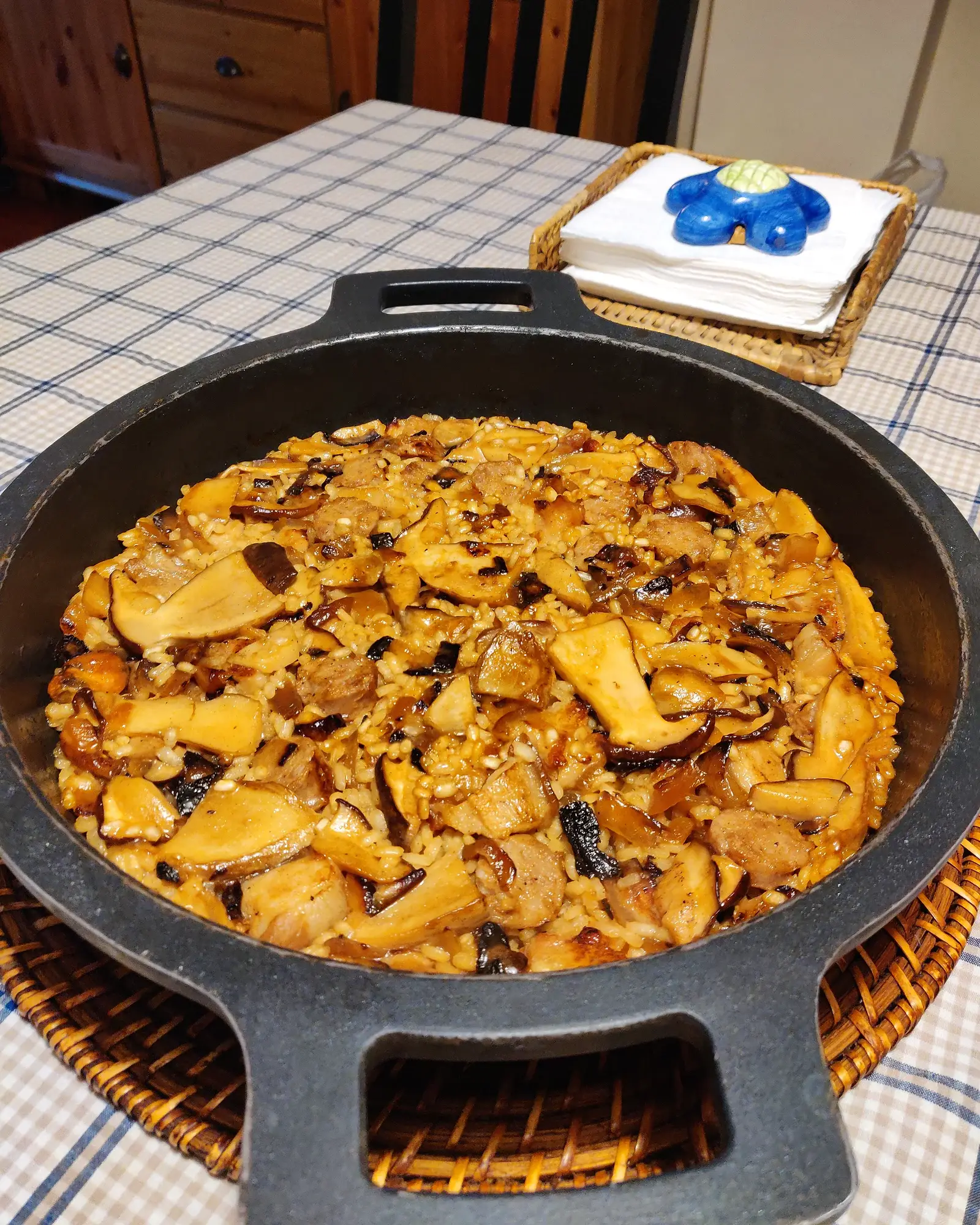 Arròs de ceps amb cansalada i botifarra acabat de fer en una paella de ferro colat amb dues nanses, sobre unes estovalles de quadres.