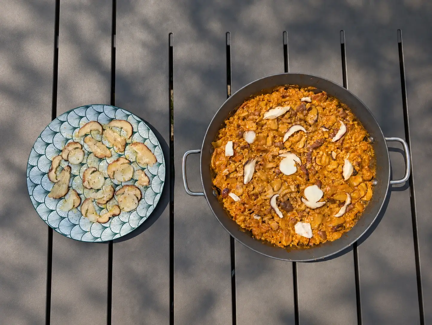 Paella d’arròs de galtes de porc amb ceps vista des de dalt, amb un plat de carpaccio de ceps al costat.
