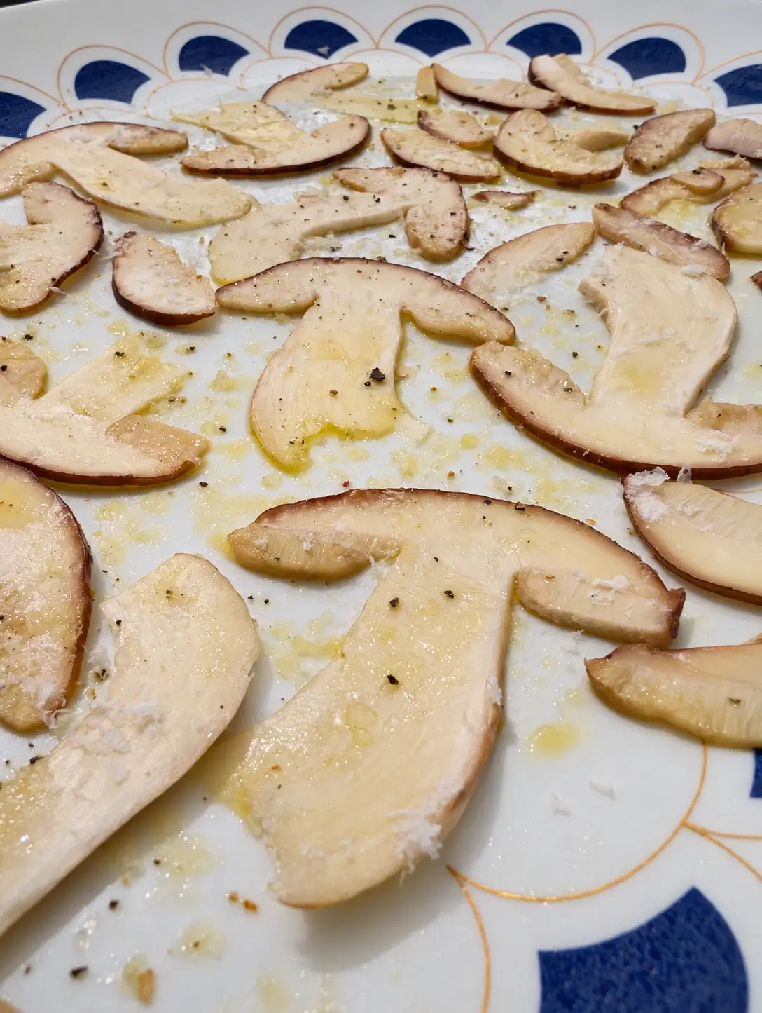 Detall de les làmines de cep amb oli, pebre i formatge, sobre una plata blanca amb mitges llunes blaves.