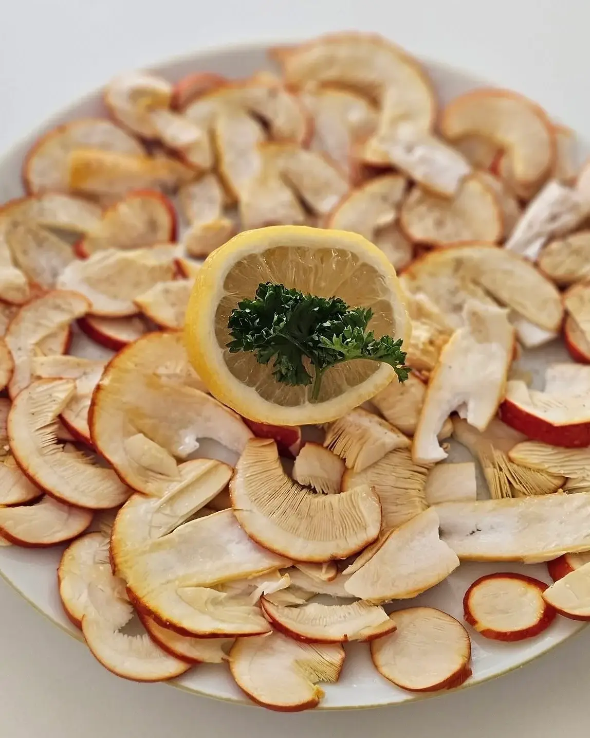 Carpaccio d’ous de reig en una plata blanca: làmines fines amb la vora taronja del barret, i una rodanxa de llimona amb julivert al centre.