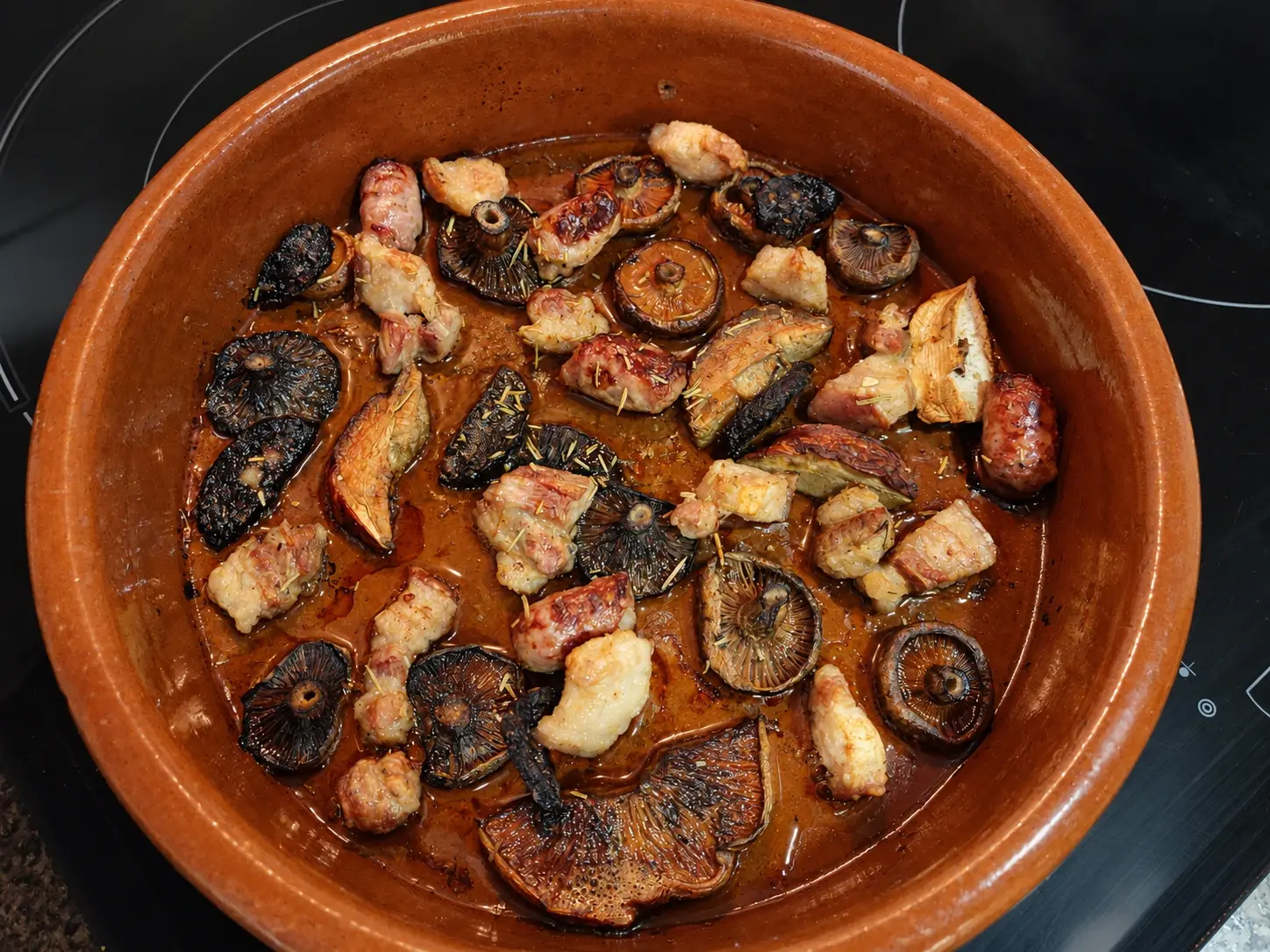 Rovellons amb cansalada i botifarra daurats en una cassola rodona de fang, amb all i herbes.