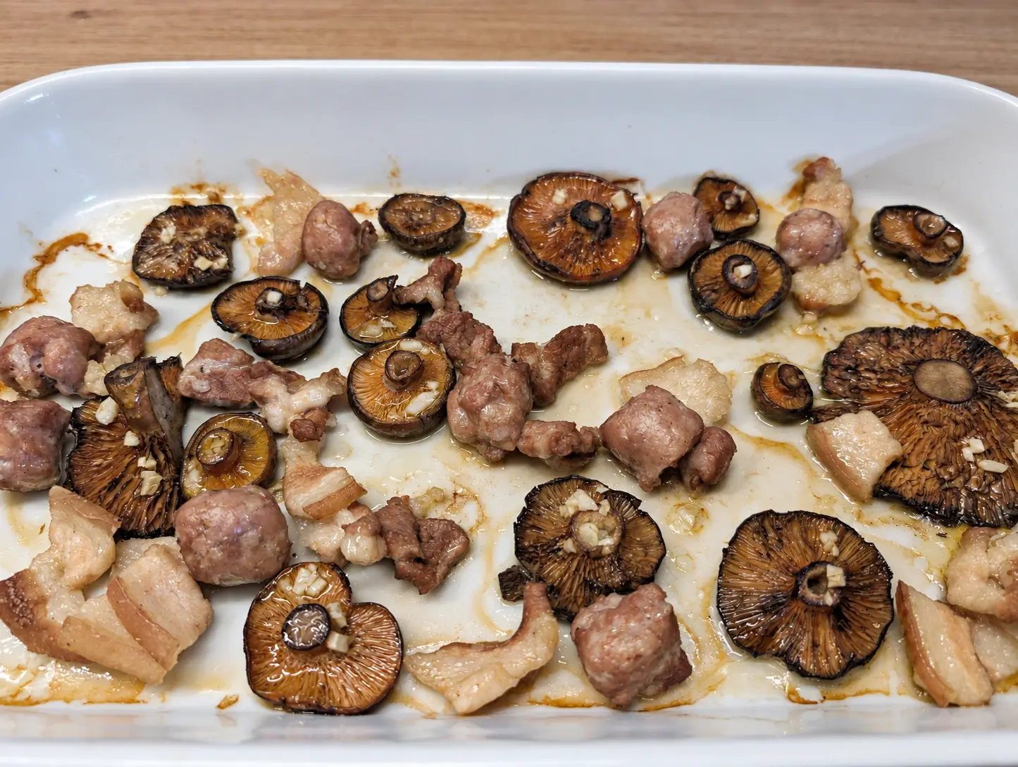 Rovellons al forn amb les làmines cap amunt i all picat, entre trossos de cansalada i de botifarra, en una safata de forn blanca.